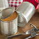 Can opener on table beside unlabeled half-open can of food